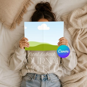 May include: A rectangular journal mockup featuring a light blue sky with white clouds and green rolling hills on the cover. The text front & back JOURNAL MOCKUP is printed in white over the center. A circular purple and blue Canva logo is visible.