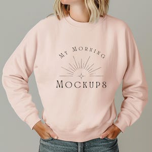 Może przedstawiać: Jasnoróżowa bluza z okrągłym dekoltem z czarnym napisem "MY MORNING MOCKUPS". Projekt zawiera grafikę w kształcie promieni słonecznych. Bluza jest jednokolorowa i ma długie rękawy.