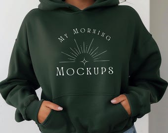 May include: A dark green hoodie with a front pocket and a hood. The hoodie features the text "MY MORNING MOCKUPS" in white, with a sunburst design. The model is wearing the hoodie.