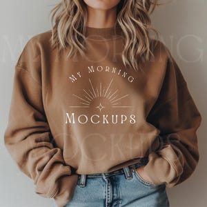 May include: A brown sweatshirt with the text "My Morning Mockups" in white lettering. The text is centered on the sweatshirt and is surrounded by a stylized sun graphic.