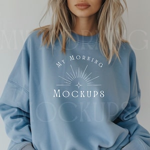 May include: A light blue sweatshirt with the text "MY MORNING MOCKUPS" in white. The design includes a sunburst graphic. The sweatshirt is a solid color and has a crew neck.