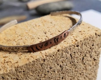 May include: A silver and copper bracelet with the words "live free" stamped on the copper band.