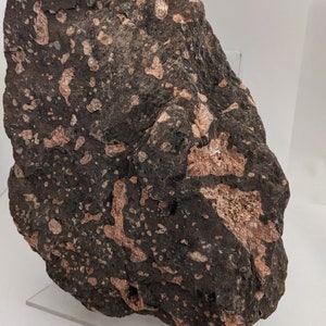 May include: A large, dark gray rock with a speckled, reddish-brown pattern. The rock has a rough, uneven surface.