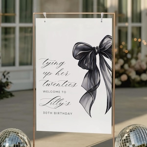 May include: A sign with the text "Tying up her twenties, Welcome to Lilly's, 30th Birthday" and a black bow illustration. The sign is in a copper-colored frame, with disco balls at the base.