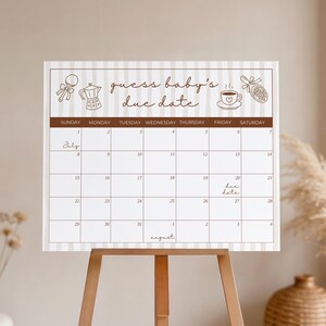 Può includere: Un cartello calendario rettangolare con sfondo a righe beige chiaro e testo marrone che recita "guess baby's due date". Il calendario presenta illustrazioni di un sonaglio, una caffettiera, una tazzina di caffè e un ciuccio, con date di luglio e agosto.