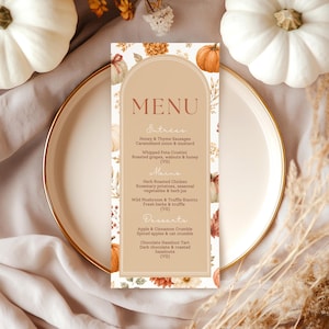 May include: A tall, rectangular menu card with an arched top, featuring a tan background and a border decorated with orange pumpkins and autumn foliage. The text reads MENU, Entrees, Mains, and Desserts with various food items listed.