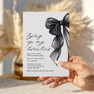 Pu&ograve; includere: Un biglietto d'invito bianco con la scritta "Tying up my twenties" e un'illustrazione di fiocco nero. La carta include anche i dettagli della festa: data, ora e luogo per il 30&deg; compleanno di Lilly.