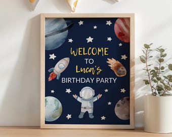 May include: A framed birthday party sign with a space theme. The navy blue background features planets, stars, a rocket, and an astronaut. The text reads "WELCOME TO Luca's BIRTHDAY PARTY" in gold and white.