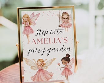 May include: A framed sign with a gold border features illustrations of fairies in pink dresses and the text "Step into Amelia's fairy garden." The sign is displayed on a wooden surface.