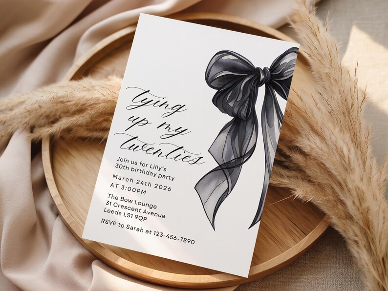 Pu&ograve; includere: Un biglietto d'invito bianco con il testo "Tying up my twenties" e i dettagli dell'evento. Una grande ed elegante illustrazione di fiocco nero adorna il lato destro. Il biglietto &egrave; appoggiato su un vassoio di legno con piante decorative essiccate.