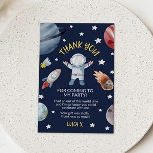 May include: A navy blue thank you card featuring an astronaut, planets, stars, and a rocket. The text says "Thank You For Coming To My Party!" with a personalized message and name.