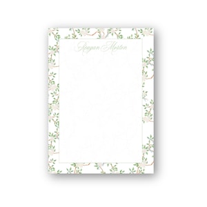 May include: White stationery with a floral border featuring white flowers and green leaves. The name "Reagan Morton" is written in a delicate green script at the top. The design is elegant and suitable for personalized notes.