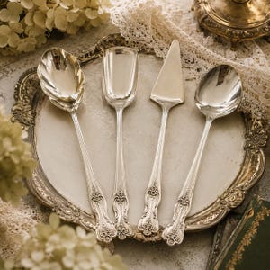 Puede incluir: Un juego de cuatro utensilios de servicio plateados que incluye una cuchara de cuenco festoneado, una cuchara rectangular de borde plano, un servidor de pasteles triangular y una cuchara ovalada estándar, con mangos florales.