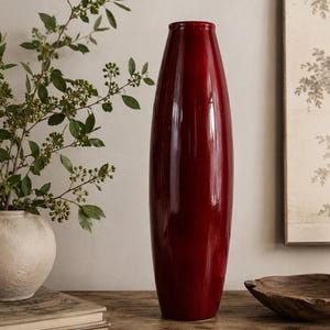 Peut inclure: Un grand vase cylindrique doté d'une finition rouge profond lisse et brillante. Le vase présente une ouverture étroite au sommet et une base légèrement effilée, se tenant droit comme un objet décoratif unique avec une surface réfléchissante.