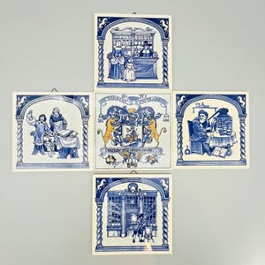 May include: Five blue and white ceramic tiles arranged in a cross formation. Each tile features a different scene, including a pharmacy, a coat of arms, and figures in historical settings. The tiles have a decorative border.