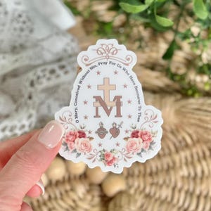 Puede incluir: Una pegatina blanca con un dise&ntilde;o floral y el texto "Oh Mar&iacute;a, concebida sin pecado, ruega por nosotros que recurrimos a ti" y una "M" estilizada con una cruz encima.