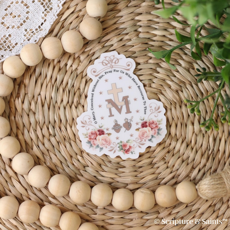 Puede incluir: Una pegatina blanca con un dise&ntilde;o floral y el texto "Oh Mar&iacute;a, concebida sin pecado, ruega por nosotros que recurrimos a ti" que rodea una imagen estilizada de la Virgen Mar&iacute;a con las letras "M" e "I" y una cruz. La pegatina tambi&eacute;n incluye un coraz&oacute;n con una espada y un coraz&oacute;n con una llama.