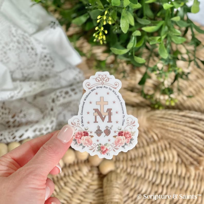 Puede incluir: Una pegatina blanca con un dise&ntilde;o floral y el texto "Oh Mar&iacute;a, concebida sin pecado, ruega por nosotros que recurrimos a ti" y una "M" estilizada con una cruz encima.