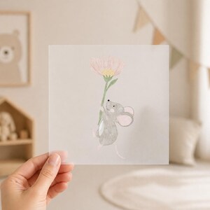 Könnte beinhalten: Quadratischer, durchscheinender Druck mit einer Illustration einer grauen Maus, die eine rosa Blume hält. Die Maus hat rosa Ohren und einen weißen Bauch. Die Blume hat eine gelbe Mitte und einen grünen Stiel. Das Kunstwerk hat eine weiche, pastellfarbene Farbpalette.