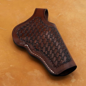 May include: A brown leather holster with a woven pattern and white stitching. The holster is designed to hold a handgun.