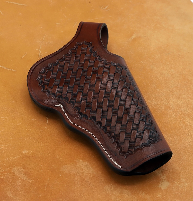 May include: A brown leather holster with a woven pattern and white stitching. The holster is designed to hold a handgun.
