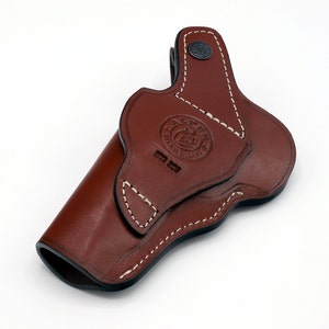 May include: A brown leather holster with white stitching and a black button. The holster has a logo that says "ALPS" and "SILAS BROTHERS".