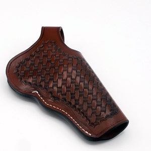 May include: A brown leather holster with a woven pattern. The holster has a white stitching detail around the edges.