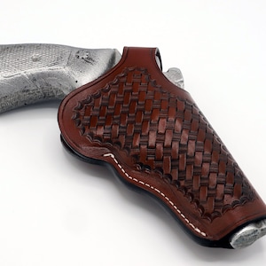 May include: A brown leather holster with a woven pattern and white stitching. The holster is designed to hold a handgun.