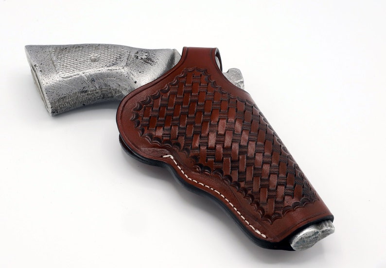 May include: A brown leather holster with a woven pattern and white stitching. The holster is designed to hold a handgun.