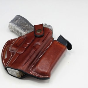 Puede incluir: Una funda de cuero marrón con una bolsa para cargador para una pistola. La funda tiene un cierre de presión y está diseñada para llevarse en un cinturón.