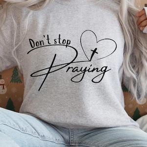 Peut inclure: Sweat-shirt gris avec le texte "Don't stop praying" et un c&oelig;ur avec une croix &agrave; l'int&eacute;rieur.