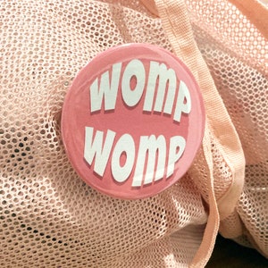 May include: A pink button with the text "Womp Womp" in white letters.