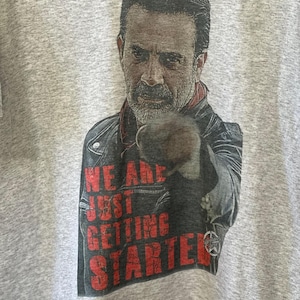 May include: A gray t-shirt with a black and white image of a man with a beard and a leather jacket. The man is pointing at the viewer and the text "We are just getting started" is printed in red below him.