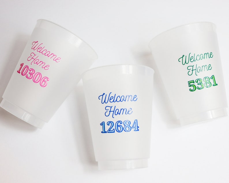 以下が含まれることがあります： 白いプラスチック製のカップが3つあり、それぞれに「Welcome Home」という言葉と番号が印刷されています。カップは白い背景の上に置かれています。番号は10306、12684、5381です。番号はピンク、青、緑の異なる色で印刷されています。