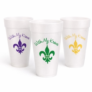 May include: Three white foam cups with the text "With My Krewe" and a fleur-de-lis design in purple, green, and yellow. The cups are likely for a Mardi Gras celebration or themed event.