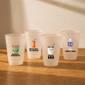 May include: Four frosted plastic cups featuring Halloween-themed cocktail illustrations and text. The designs include a green drink labeled Midnight Margaritas, an orange drink labeled Witch Way To The Bar, a white ghost drink labeled Sip Sip Boo, and a purple skull drink labeled Creep It Real.