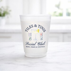 May include: A frosted plastic cup with the words "TILES & TINIS Social Club" printed in navy blue. The design includes a cocktail illustration and Mahjong tile graphics. The bottom of the cup reads "BAMS, CRAKS & COCKTAILS."