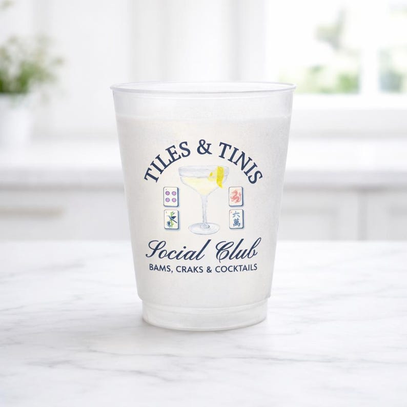 May include: A frosted plastic cup with the words "TILES & TINIS Social Club" printed in navy blue. The design includes a cocktail illustration and Mahjong tile graphics. The bottom of the cup reads "BAMS, CRAKS & COCKTAILS."