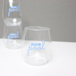 May include: Three clear plastic wine glasses with the text "At the pool" printed in blue on the front of each glass.