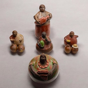 Puede incluir: Cinco figuritas de cerámica de personas, cada una con una pose diferente y sosteniendo un objeto diferente. Las figuritas están pintadas en varios tonos de marrón, rojo y verde.