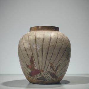 Pode incluir: Um vaso de cerâmica redondo com corpo na cor creme apresentando texturas verticais caneladas. A superfície exibe uma cena pintada de dois pássaros em voo sobre um sol escuro nascendo acima de uma linha do horizonte, com borda em tom bronze.