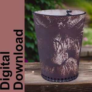 Könnte beinhalten: Eine braune Leder-Tasse mit einem weißen Design eines bärtigen Männergesichts. Die Tasse steht auf einer Holzoberfläche.