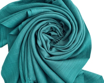 Könnte beinhalten: Ein teal-farbener Schal mit Fransen ist spiralförmig angeordnet. Der Stoff hat ein strukturiertes Aussehen, und der Schal wird vor einem weißen Hintergrund präsentiert. Die Farbe des Schals ist ein lebendiges Teal, und der Stoff scheint leicht zu sein.
