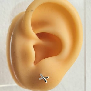 May include: A close-up of a silver cross earring worn in the lobe of an ear.