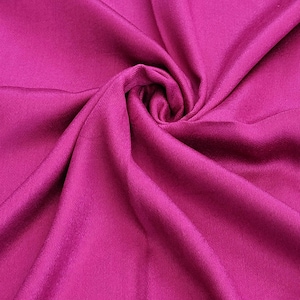 May include: A close-up of a deep pink fabric with a smooth, silky texture. The fabric is folded and draped, creating soft folds and curves.