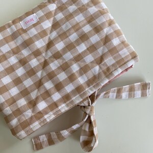 Könnte beinhalten: Gesteppte Mütze mit braun-weißem Vichy-Karo-Muster. Die Mütze hat ein rosa Innenfutter und einen passenden Bindebandverschluss. Ein kleines rosa Etikett mit dem Wort "leni" ist aufgenäht.