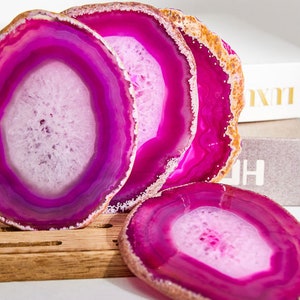 May include: Four pink agate coasters with white and purple banding. The coasters are arranged in a stack with the largest on the bottom and the smallest on top.