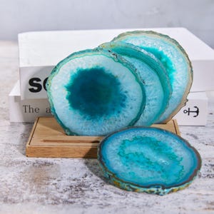 May include: Four blue and white agate coasters with a natural, organic design. The coasters are arranged on a small wooden tray, with a book in the background. The coasters have a polished surface and a unique, natural pattern.