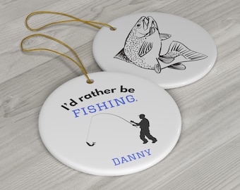 Op de afbeelding: Twee ronde keramische ornamenten met een witte achtergrond. Een ornament heeft een zwart silhouet van een vis die uit het water springt. Het andere ornament heeft een zwart silhouet van een persoon die vist met de tekst "I'd rather be FISHING." en de naam "DANNY" onder het silhouet.