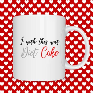 May include: White ceramic mug with the text "I wish this was Diet Coke" in black, grey, and red. The mug has a white handle and is set against a red background with white heart shapes.